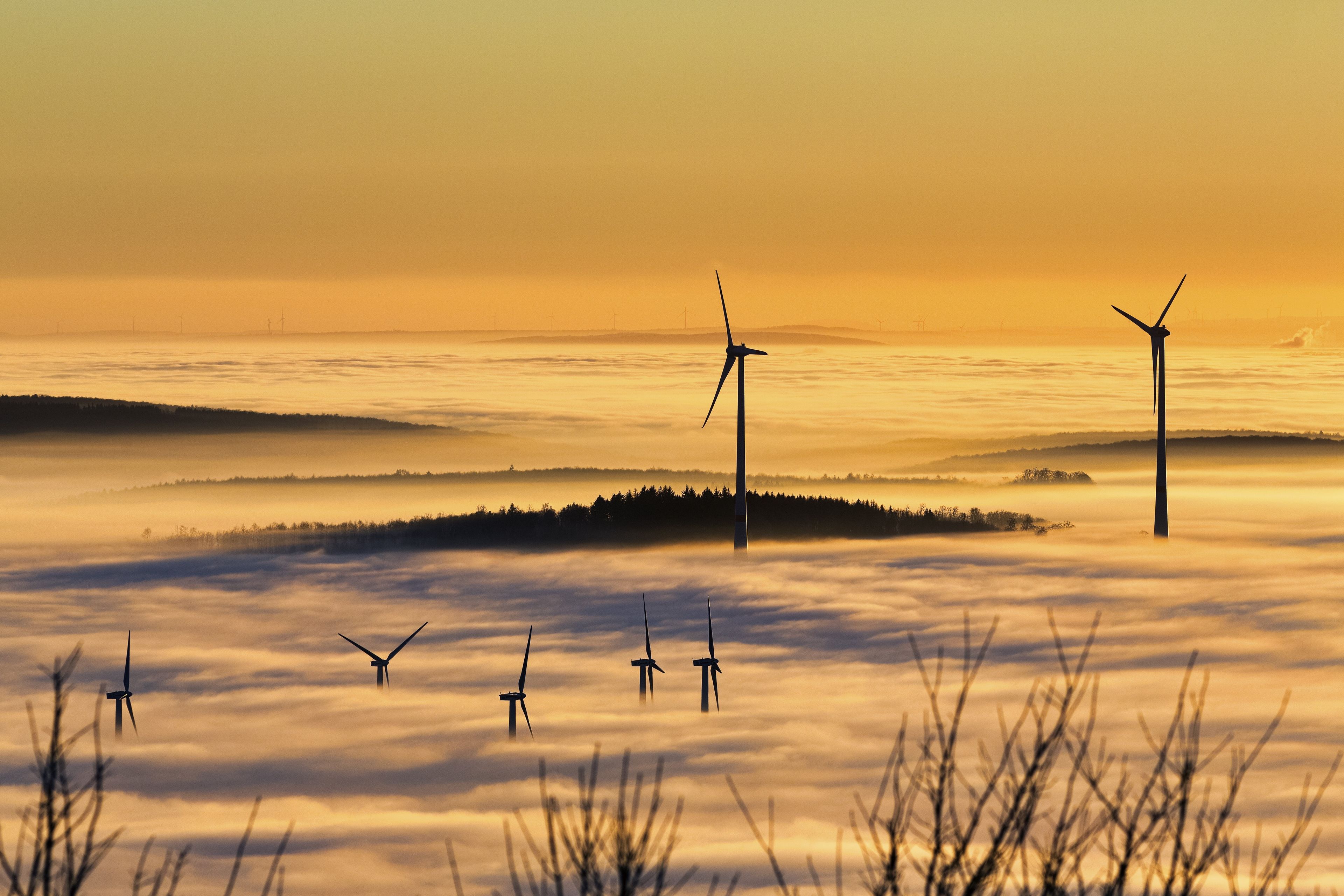 A landscape with wind turbines silhouetted against a sunrise, surrounded by a sea of clouds.