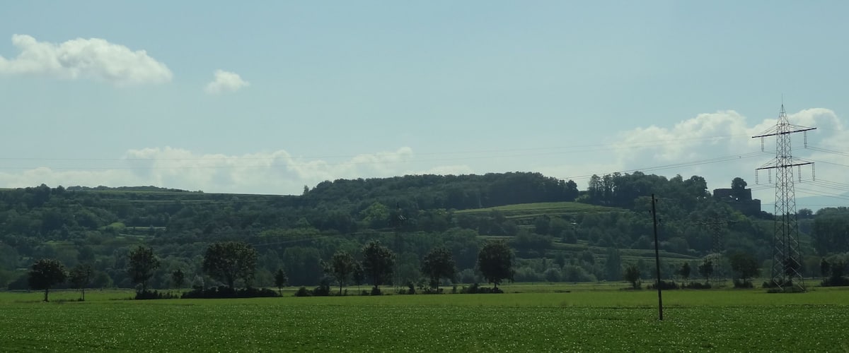 A green field with a power line tower and rolling hills in the background.
