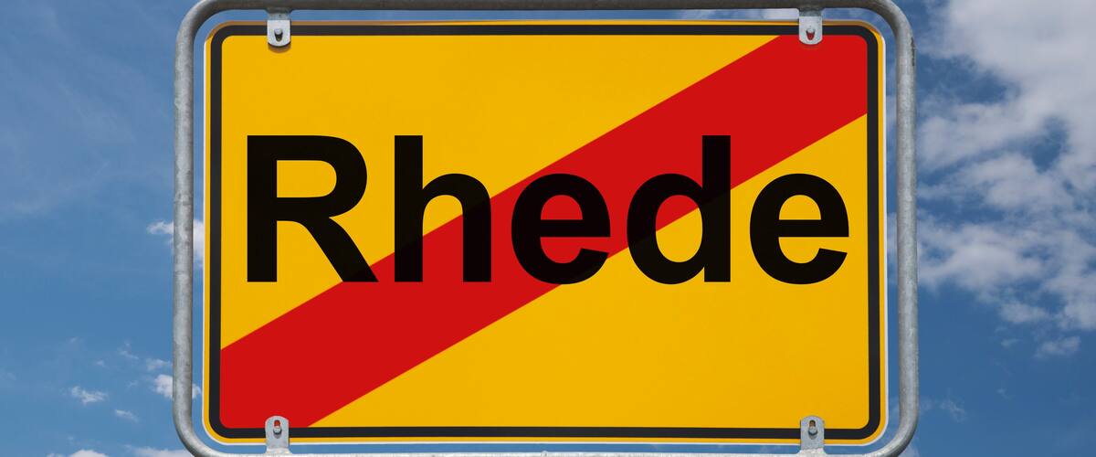 A road sign with the word "Rhode" partially visible against a blue sky with clouds.