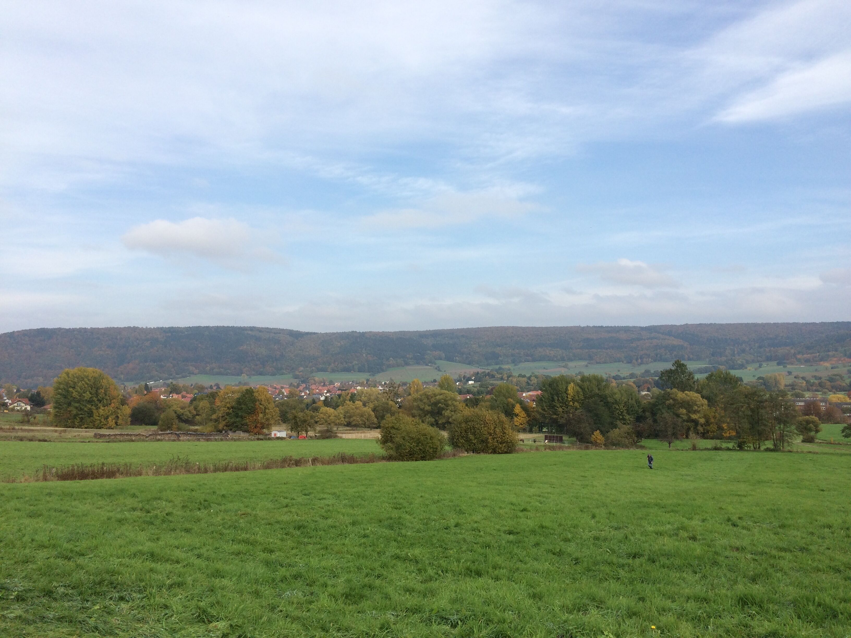 A green field with a village in the background and hills in the distance.