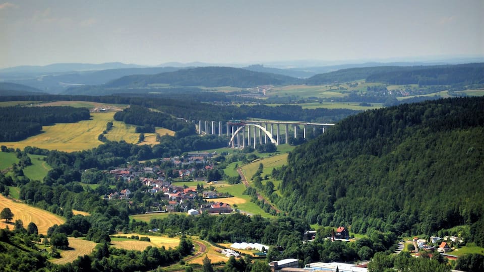 A bridge over a river, surrounded by green hills and a small town.