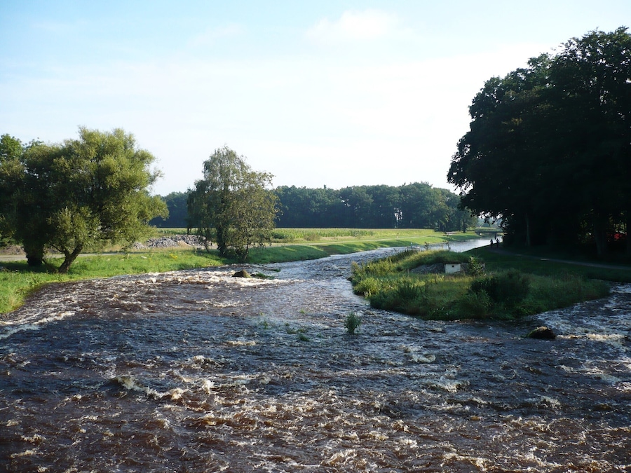 A river flowing through a rural landscape with trees and grassy fields.