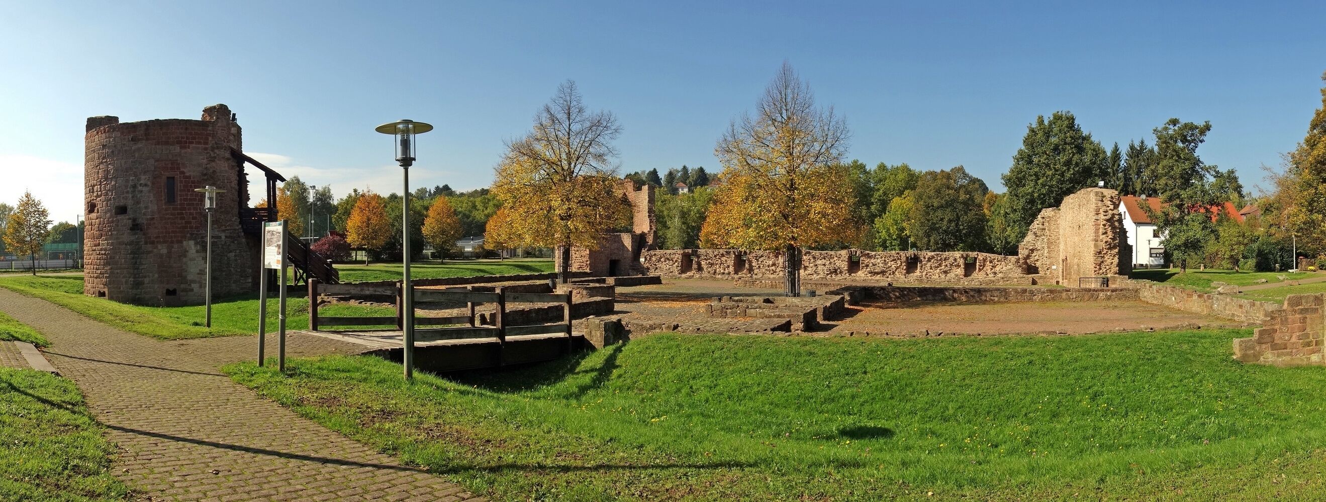 A historical site with stone ruins, a paved pathway, and a grassy area with trees.