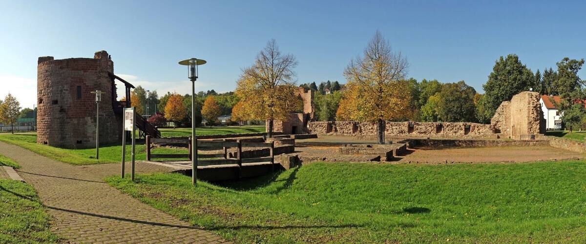 A historical site with stone ruins, a paved pathway, and a grassy area with trees.