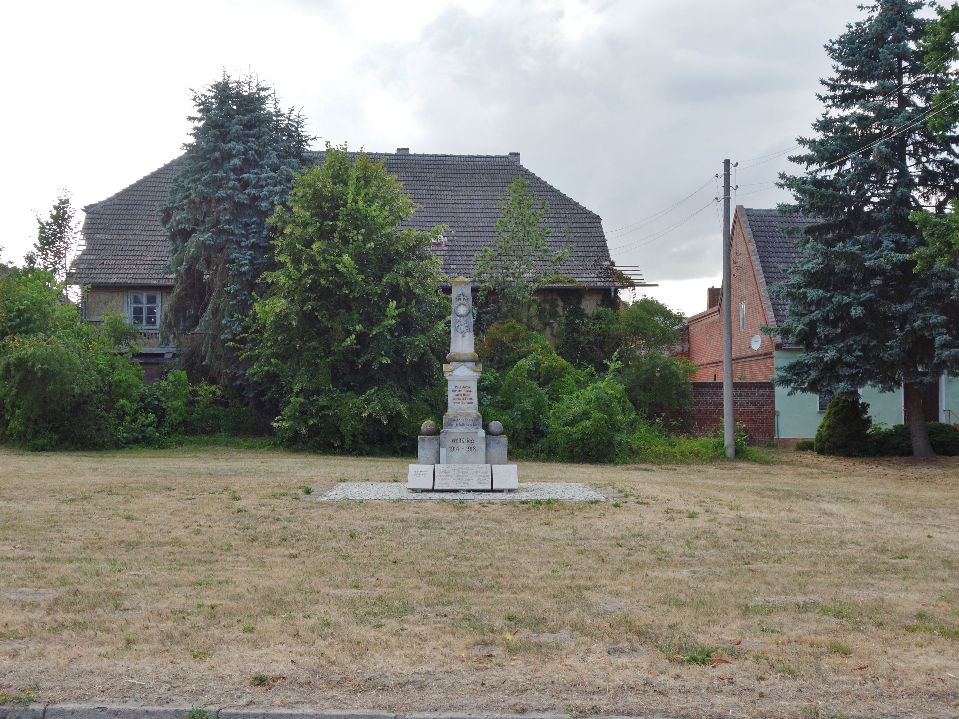 A monument in a grassy field with trees and houses in the background.