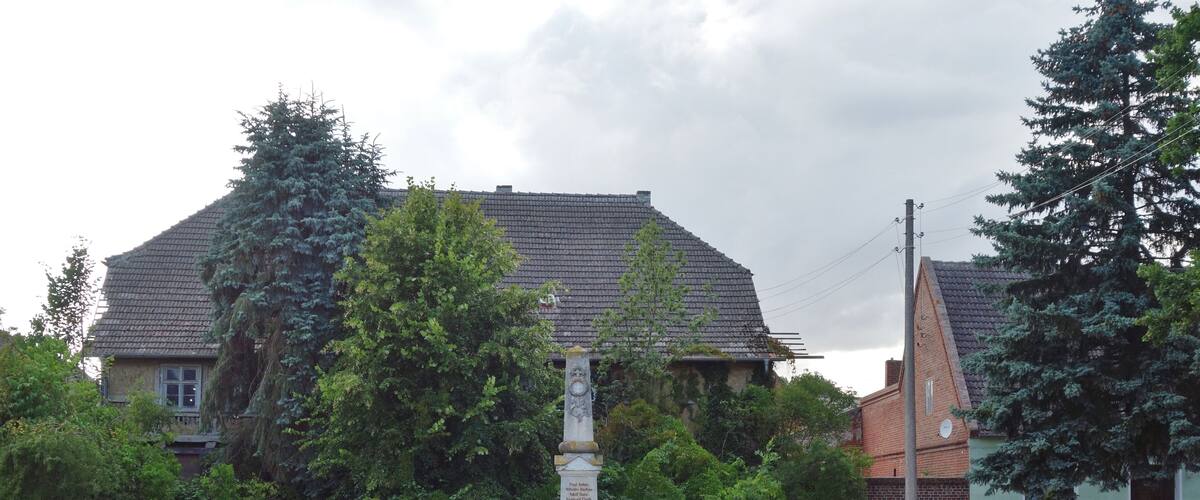 A monument in a grassy field with trees and houses in the background.