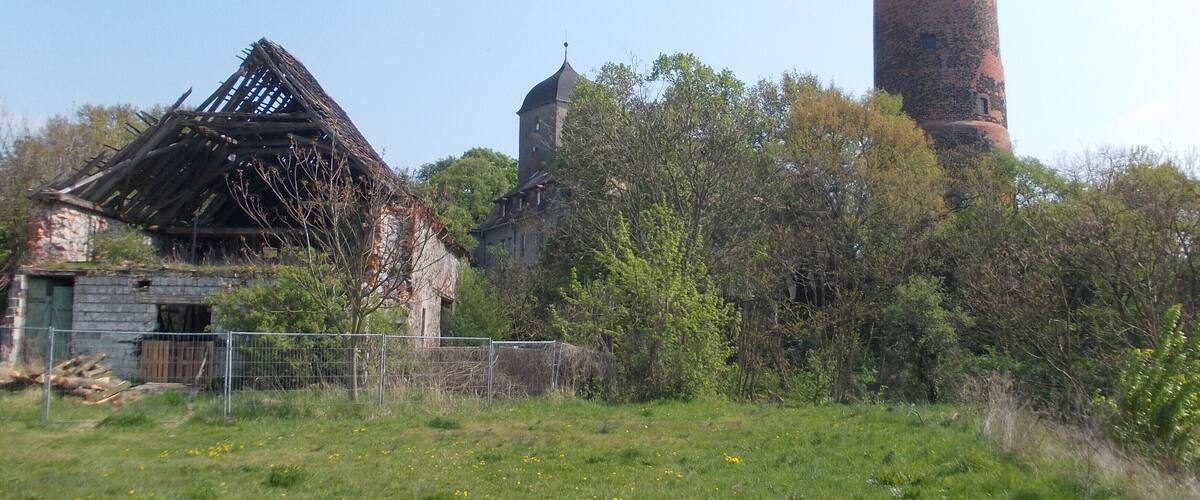 A dilapidated building with a collapsed roof, a stone tower, and a brick chimney.
