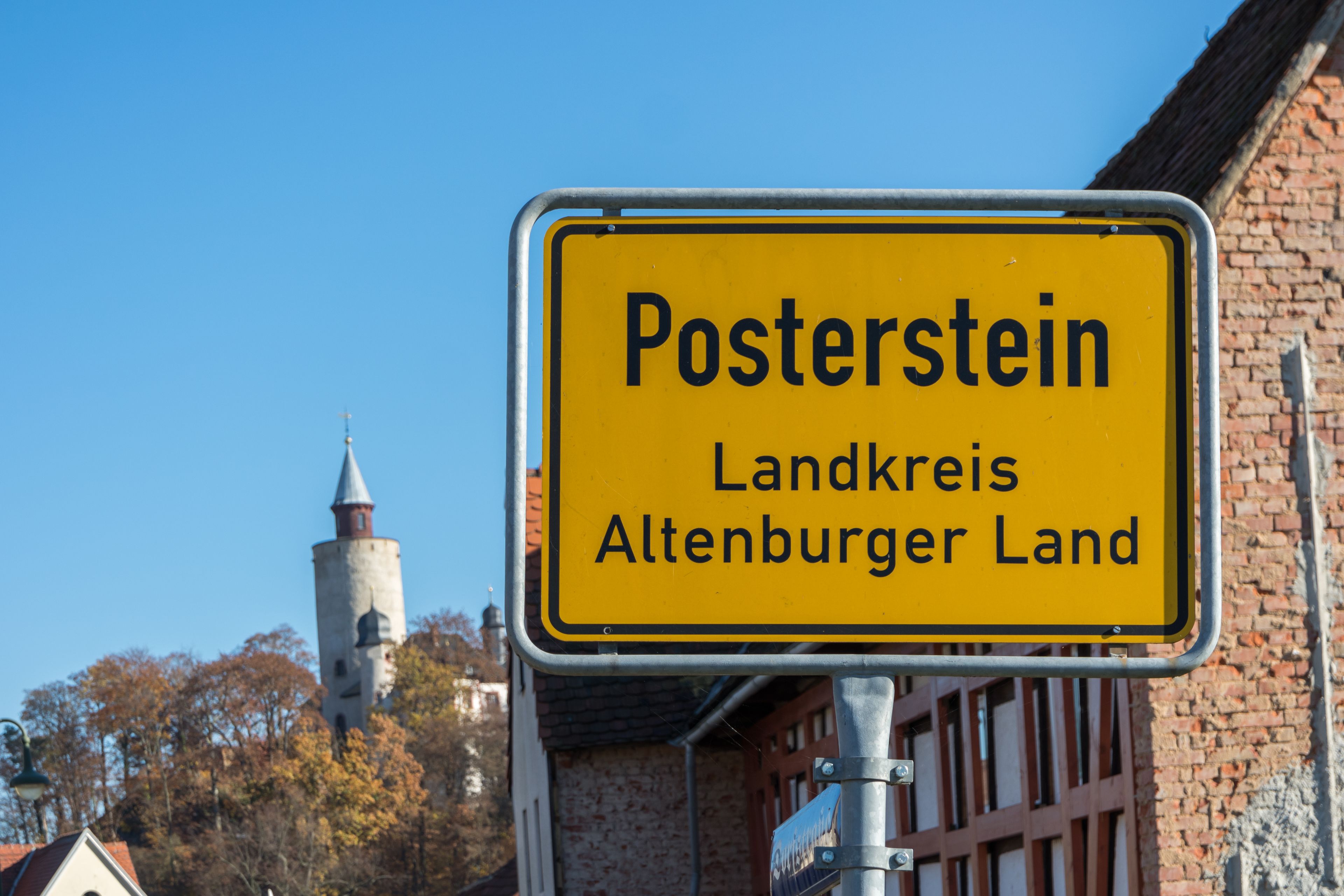 Un letrero amarillo con la leyenda 'Posterstein' y 'Landkreis Altenburger Land', sujeto a un poste de metal.