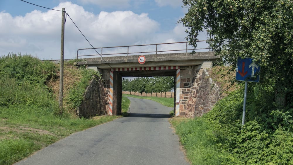 A narrow road under a stone bridge with a 30 mph speed limit sign and a directional sign.