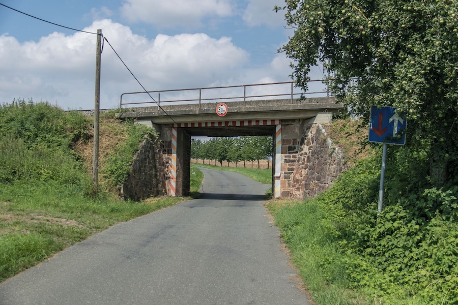 A narrow road under a stone bridge with a 30 mph speed limit sign and a directional sign.