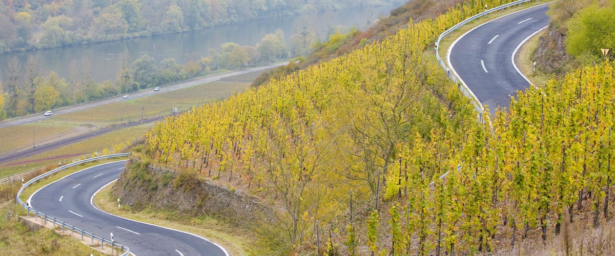 A winding road through a hilly area with a lake and autumn-colored trees.