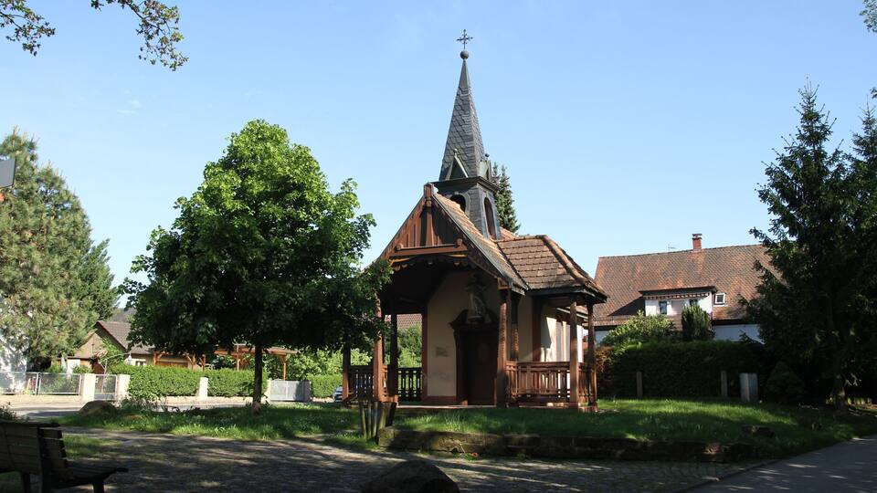 A small church with a steeple, surrounded by trees and a cobblestone path.