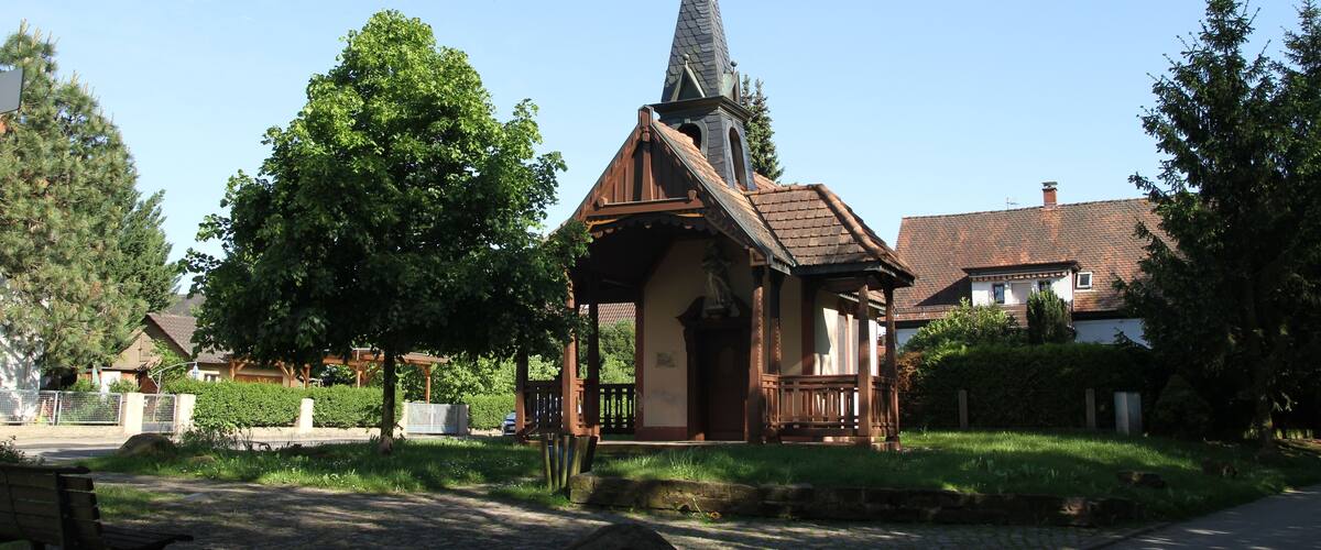 A small church with a steeple, surrounded by trees and a cobblestone path.