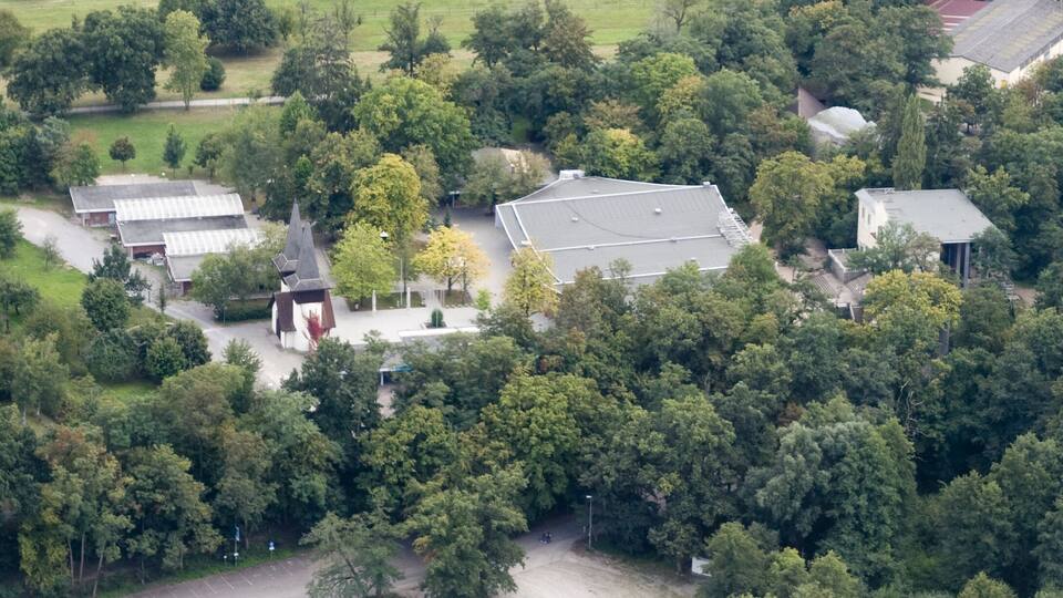 An aerial view of a residential area with houses, a church, and surrounding greenery.