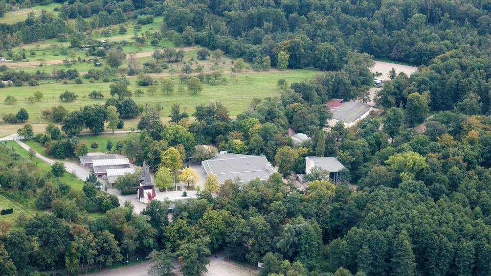 An aerial view of a rural area with a large building surrounded by dense forests and open fields.