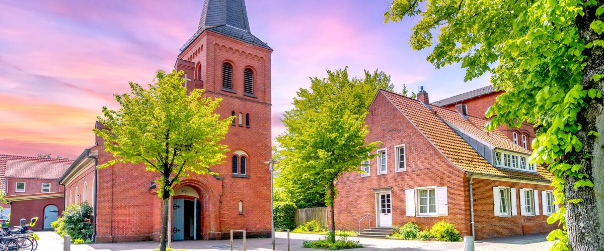 A church with a tall spire, surrounded by brick buildings and trees.