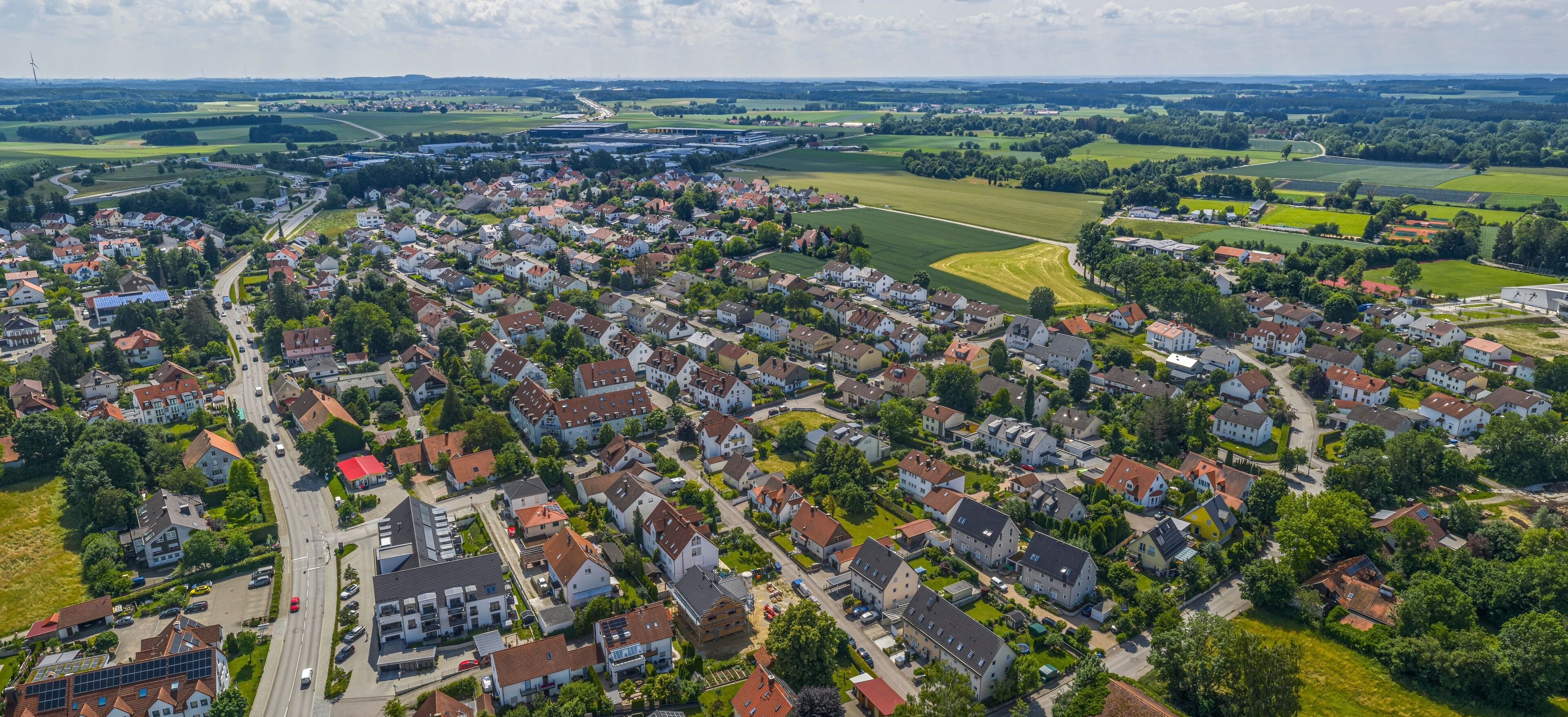 An aerial view of a residential area with houses, roads, and green fields.