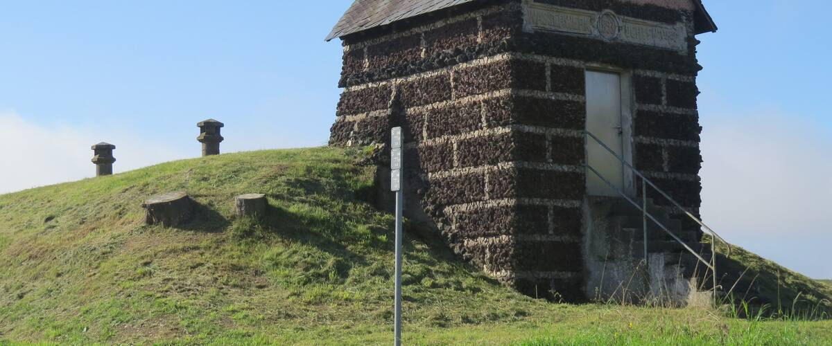 A stone building with a steep roof on a grassy hill.