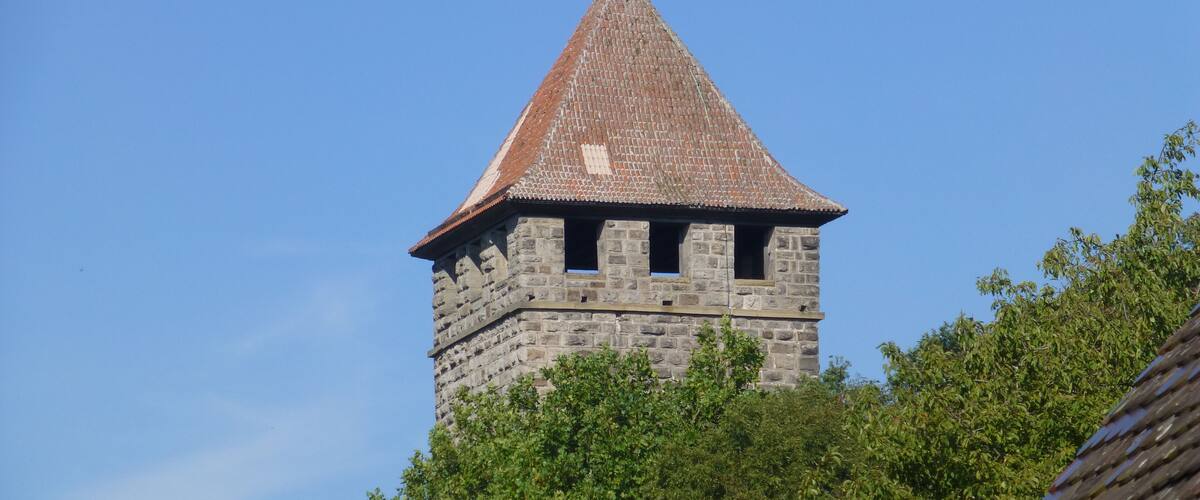 A stone tower with a conical roof, surrounded by dense green foliage.