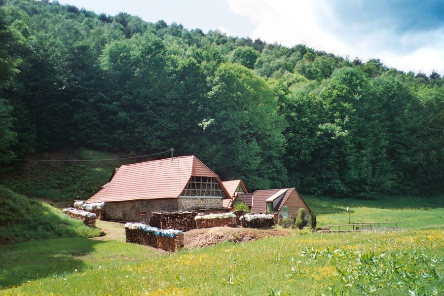 A rural landscape with a stone barn and hay bales, surrounded by lush green hills.
