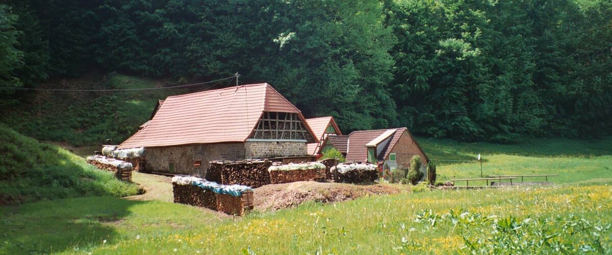 A rural landscape with a stone barn and hay bales, surrounded by lush green hills.