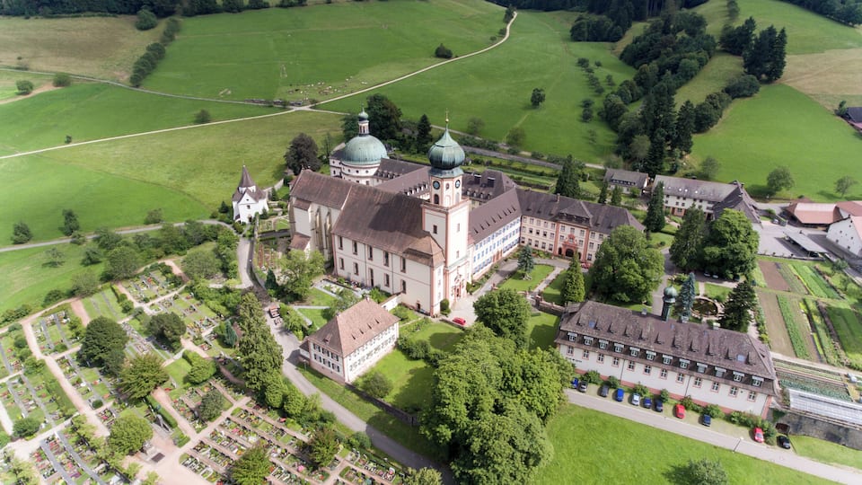 An aerial view of a historic estate with a large church, a bell tower, and expansive green fields.