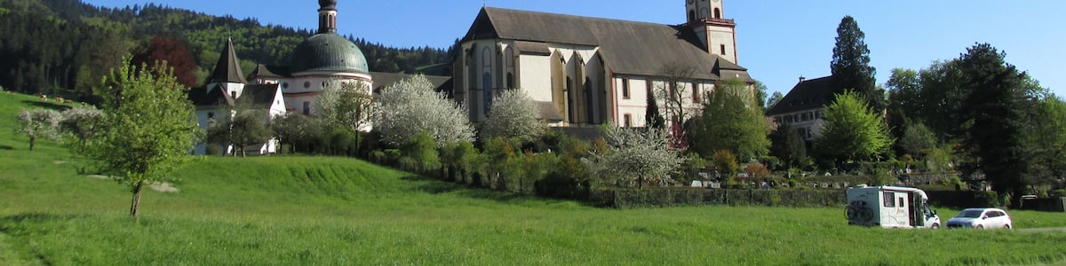 Une église dotée d’un clocher et d’une coupole, entourée de champs verdoyants et d’arbres.