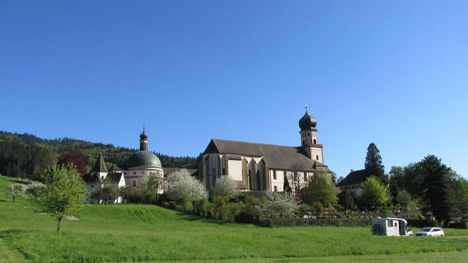 A church with a bell tower and a dome, surrounded by green fields and trees.