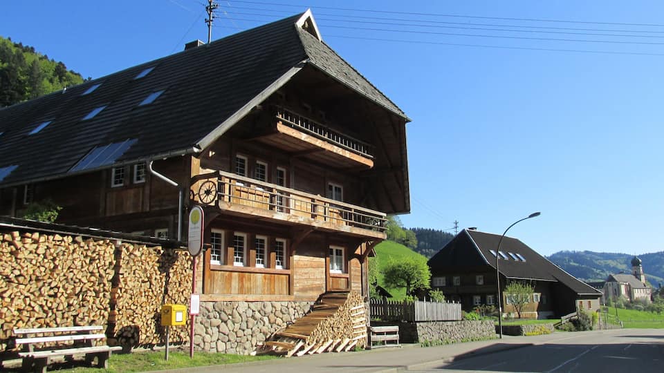 A wooden house with a balcony, a stone wall, and a wooden fence.