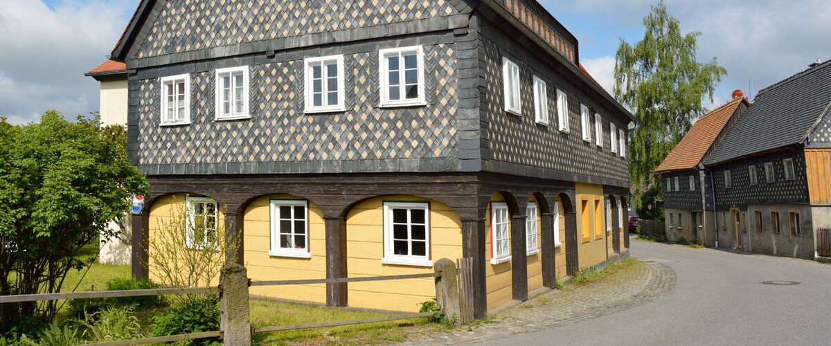 A traditional half-timbered house with a red-tiled roof, arched windows, and a cobblestone street.
