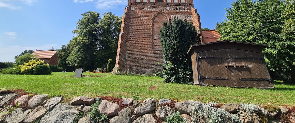 A brick church with a pointed roof and a bell tower, surrounded by a stone wall and greenery.