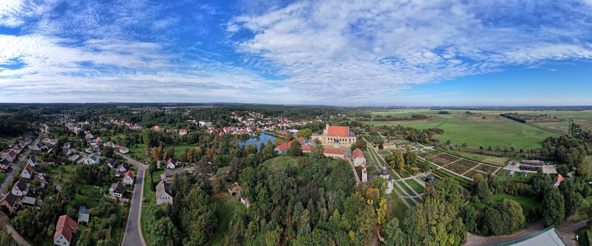 An aerial view of a town with a large church, a lake, and surrounding greenery.