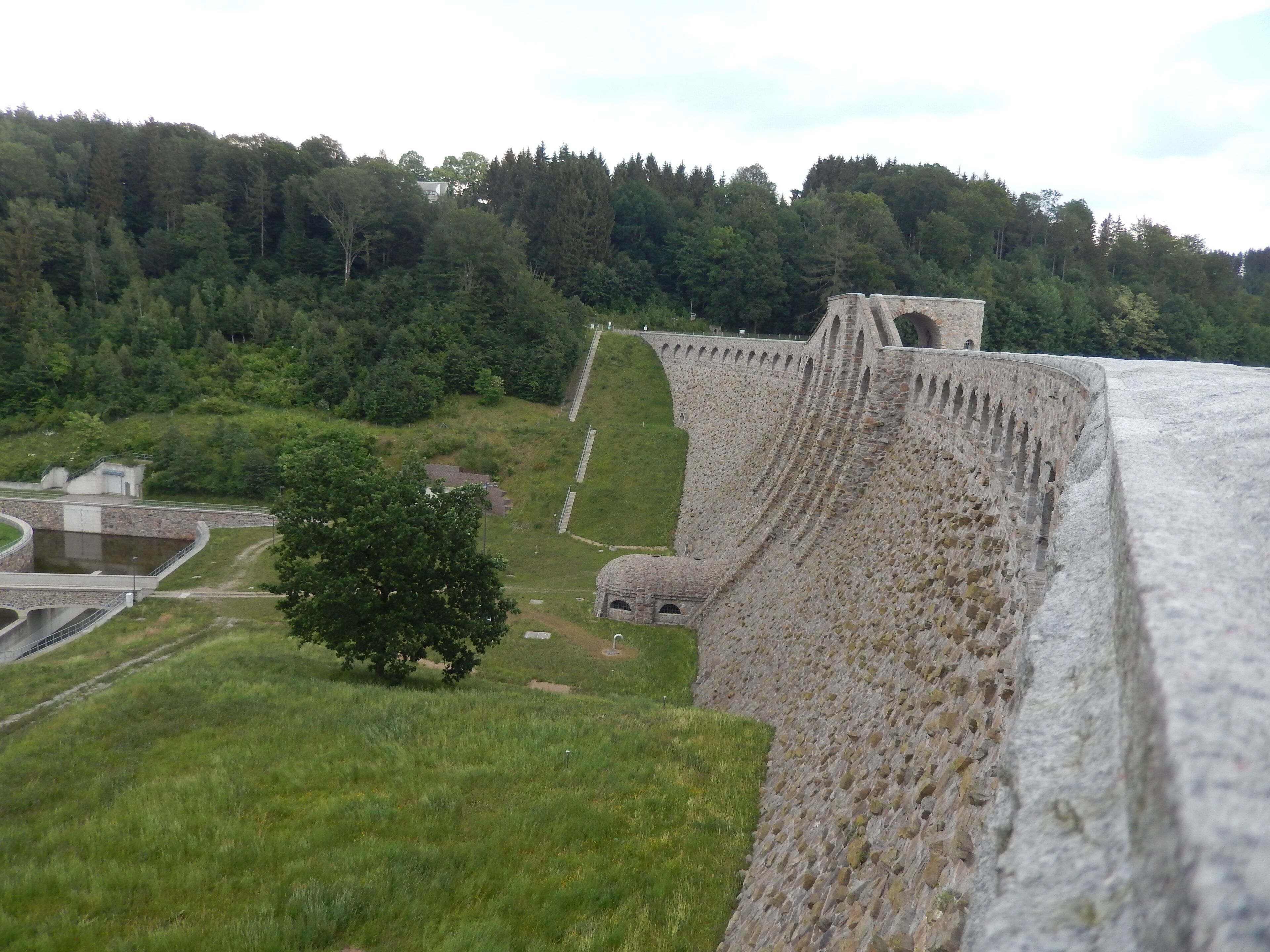 A large stone dam with a small tower, surrounded by lush green forest.