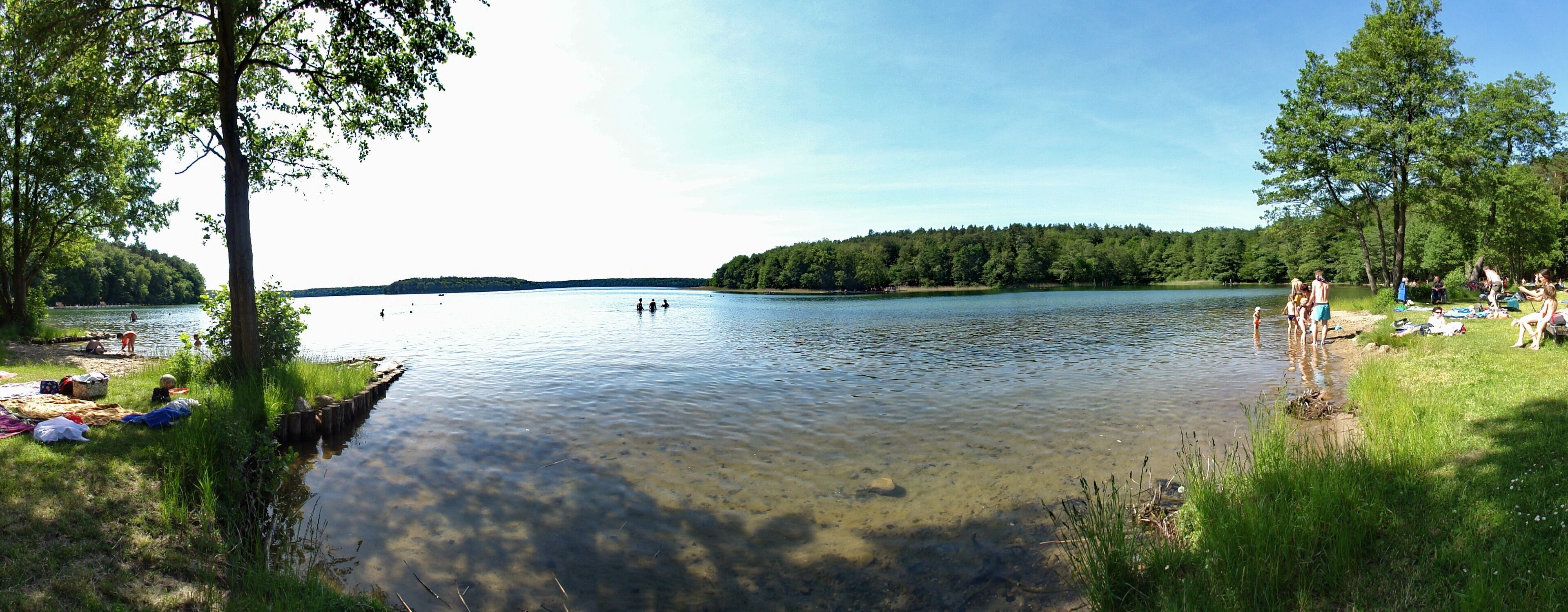 A calm lake surrounded by trees and grassy areas with people enjoying the outdoors.
