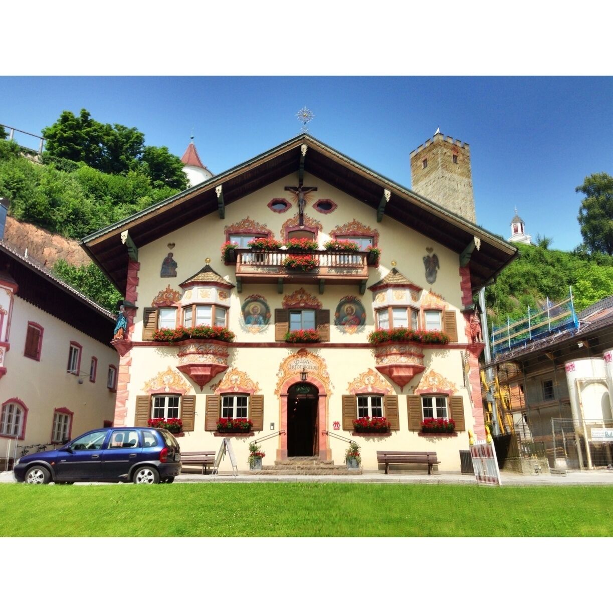 A traditional Alpine-style building with ornate balconies, a cross at the entrance, and a tower in the background.
