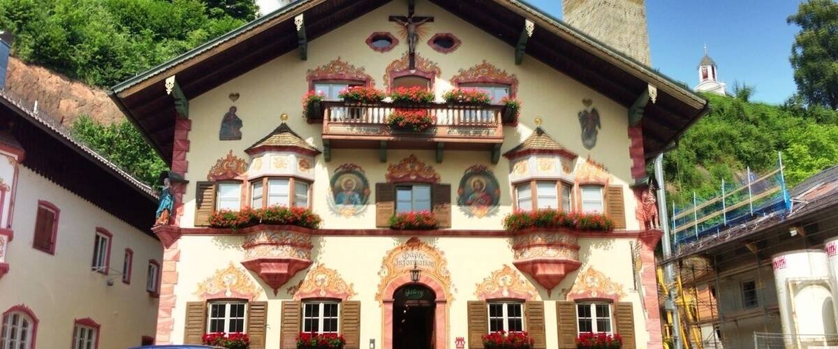 A traditional Alpine-style building with ornate balconies, a cross at the entrance, and a tower in the background.