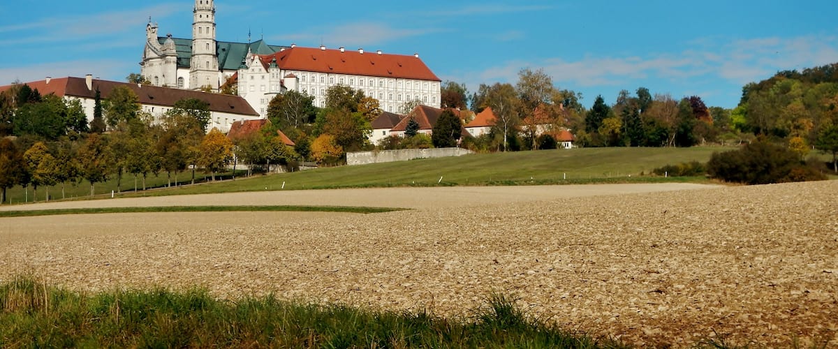 A historic building with a tower, surrounded by trees and fields.