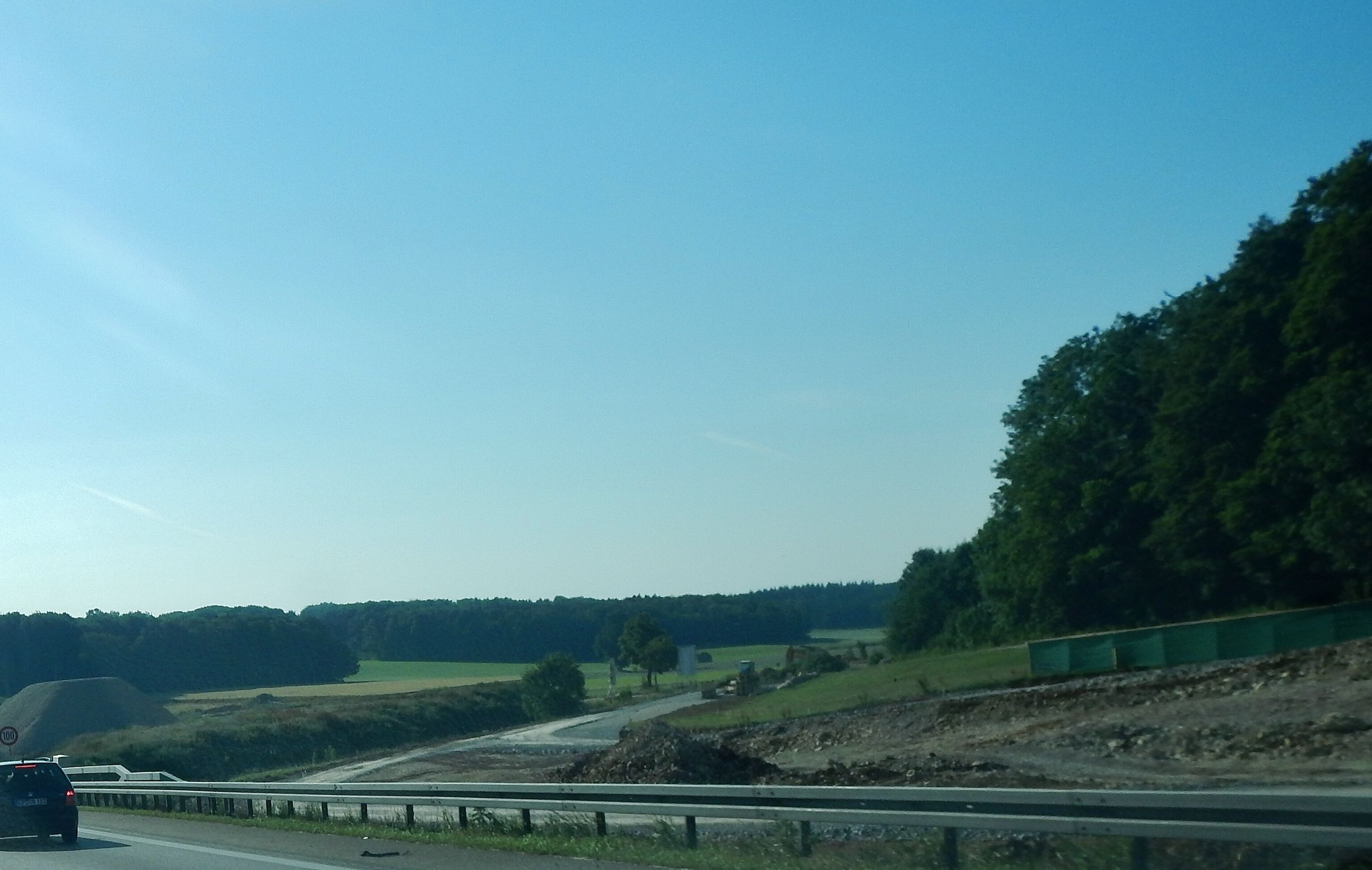 A highway with a speed limit sign, a car, and a green barrier.