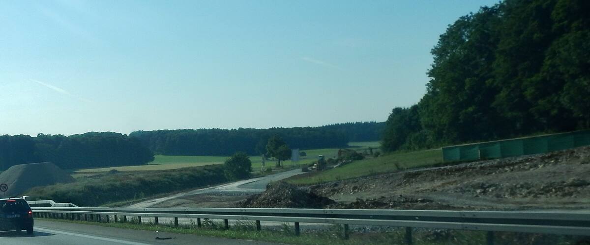 A highway with a speed limit sign, a car, and a green barrier.