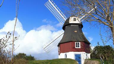 A traditional windmill on a grassy hill with a clear blue sky.