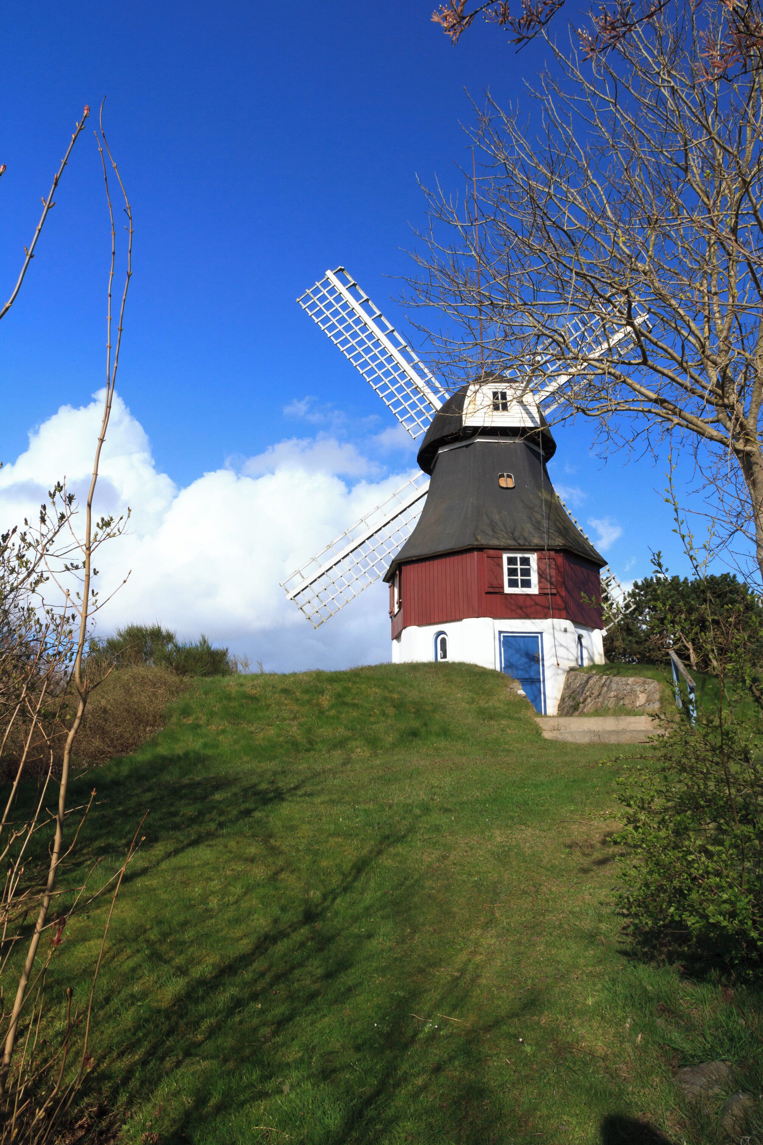 A traditional windmill on a grassy hill with a clear blue sky.