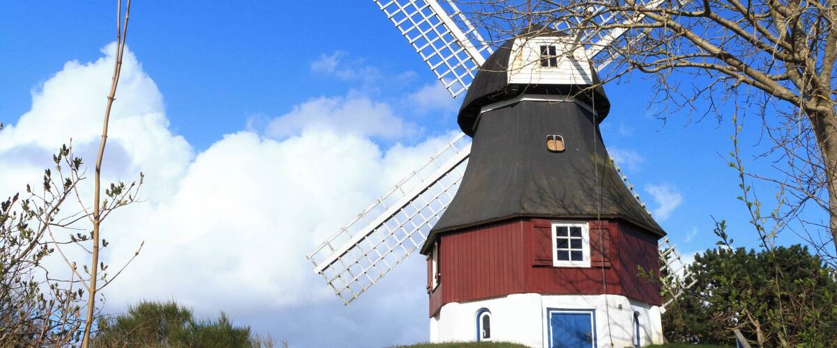 A traditional windmill on a grassy hill with a clear blue sky.