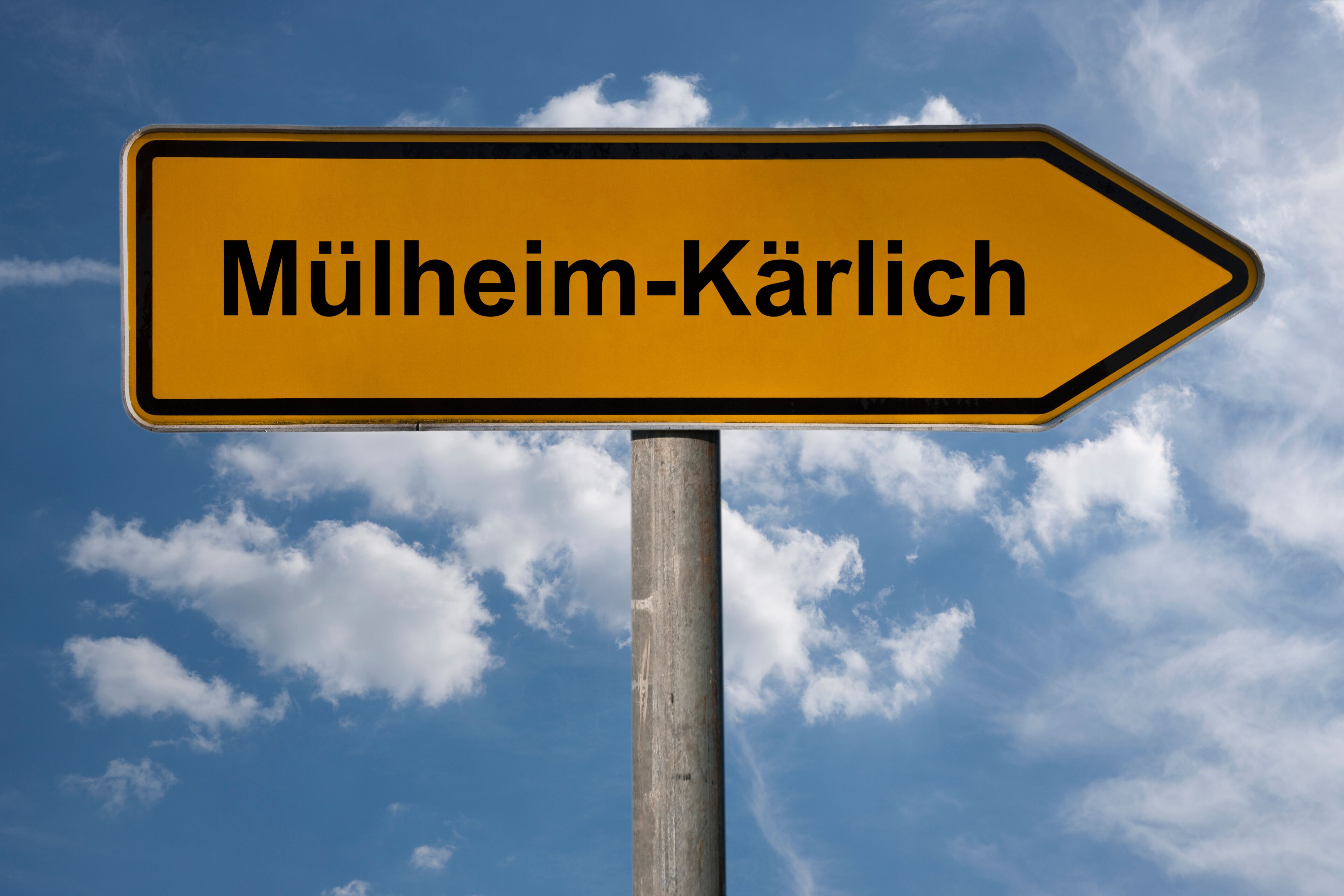 A directional sign with the text "Mülheim-Kärlich" against a blue sky with clouds.