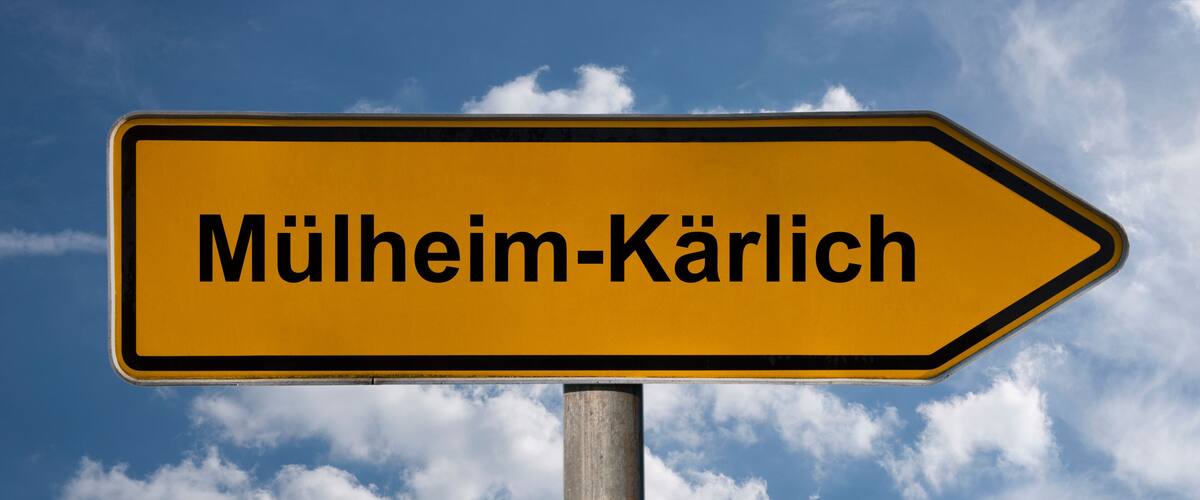 A directional sign with the text "Mülheim-Kärlich" against a blue sky with clouds.