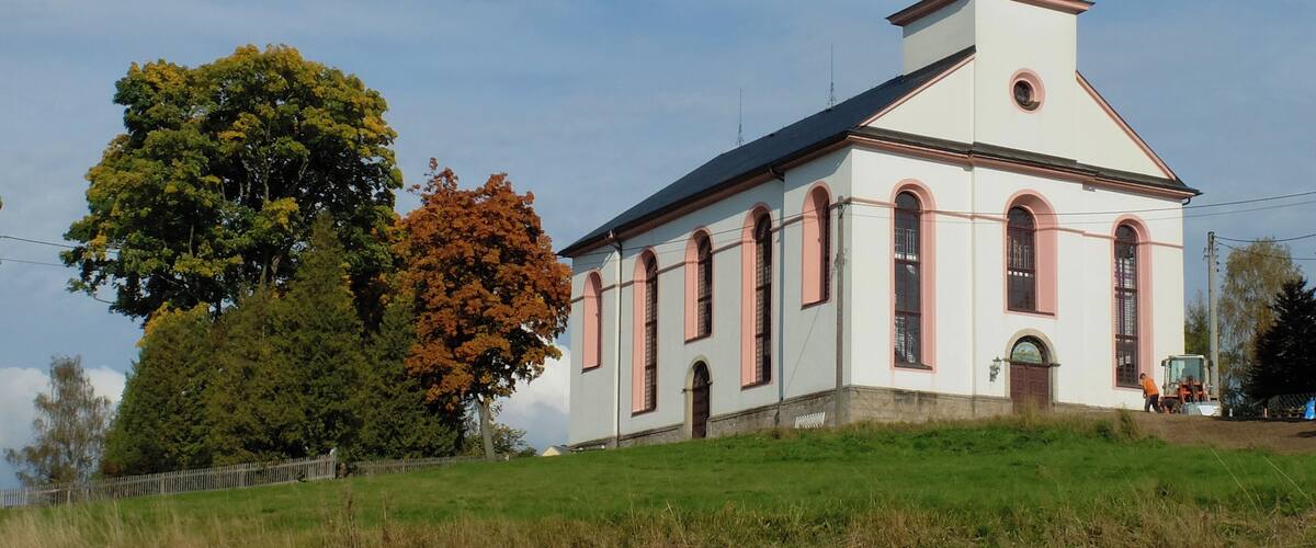 A church with a clock tower, surrounded by trees and a grassy field.