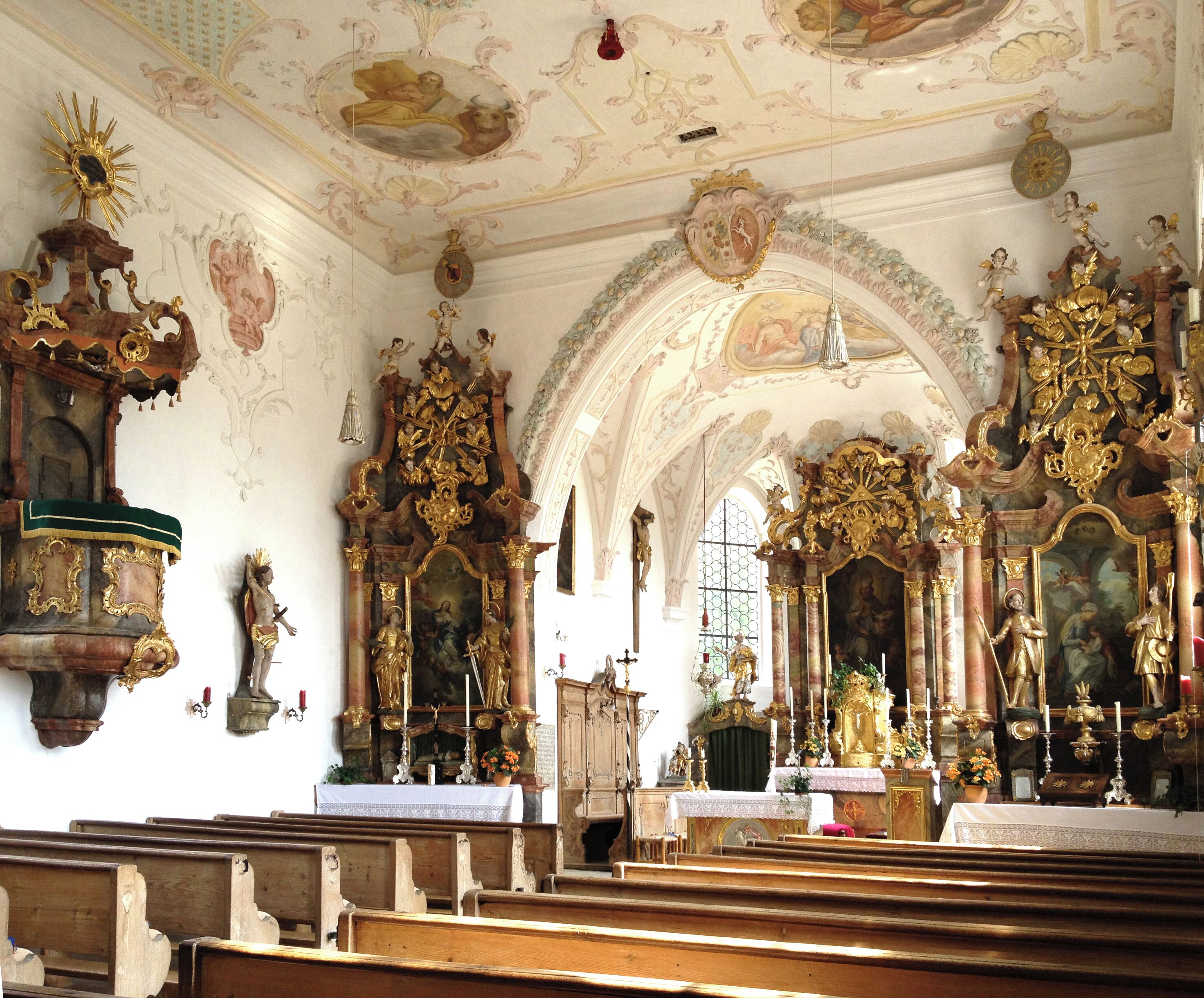 An ornate church interior with elaborate woodwork, gilded altars, and a high ceiling with frescoes.