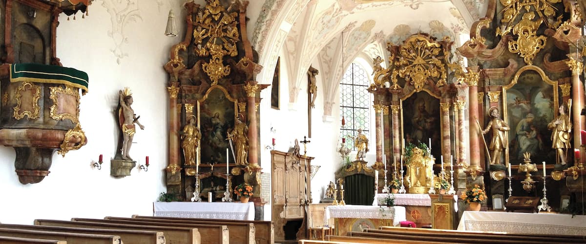An ornate church interior with elaborate woodwork, gilded altars, and a high ceiling with frescoes.