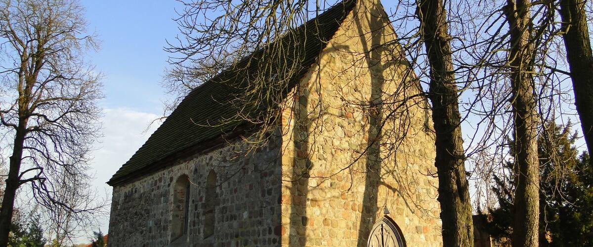 A stone church with a pointed roof, surrounded by trees and a grassy area.