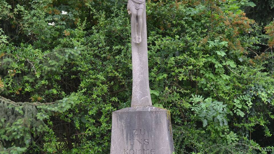 A cross with Jesus Christ, surrounded by greenery and flowers.