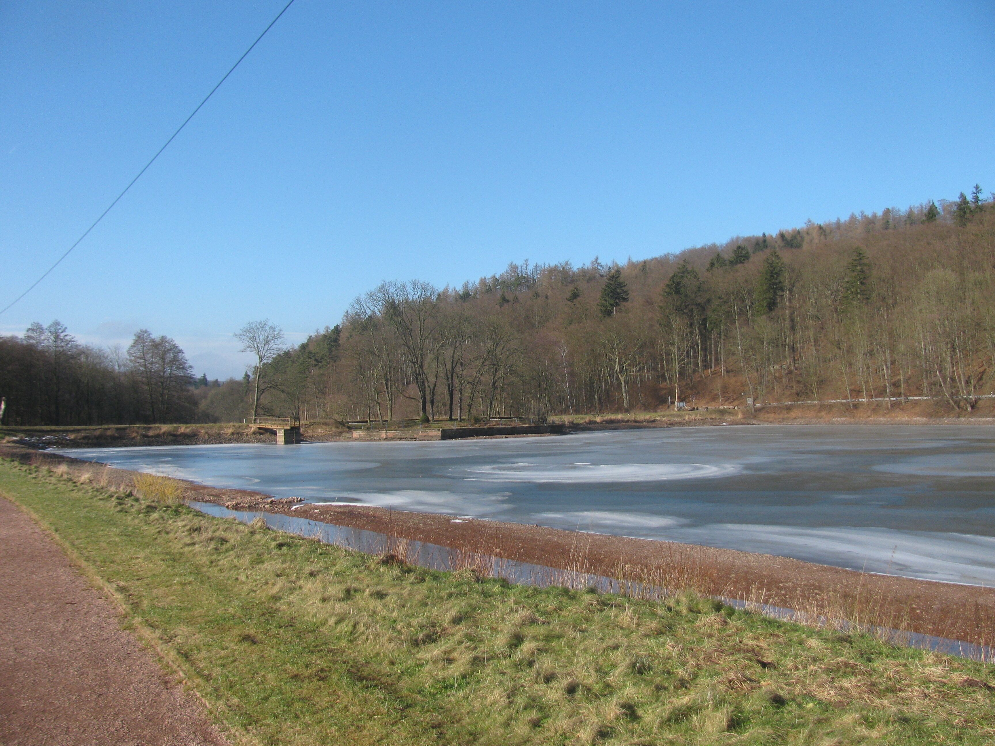 A frozen river with a bridge, surrounded by trees and grassy banks.